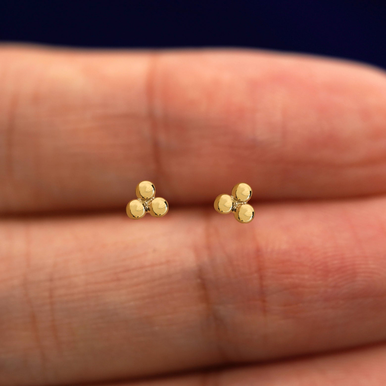 A pair of solid 14k yellow gold Ball Trio Flatback Piercing in between a model's fingers