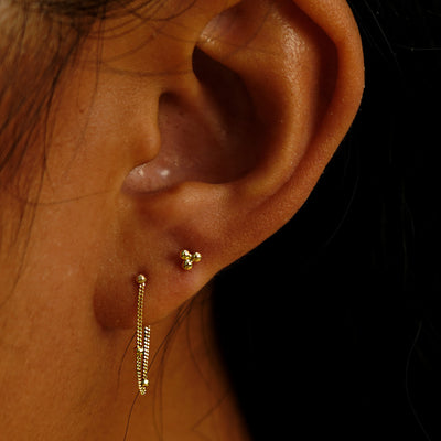 A model's ear wearing a Ball Trio stud Earring and a Bead Chain Loop Earring in two lobe piercings