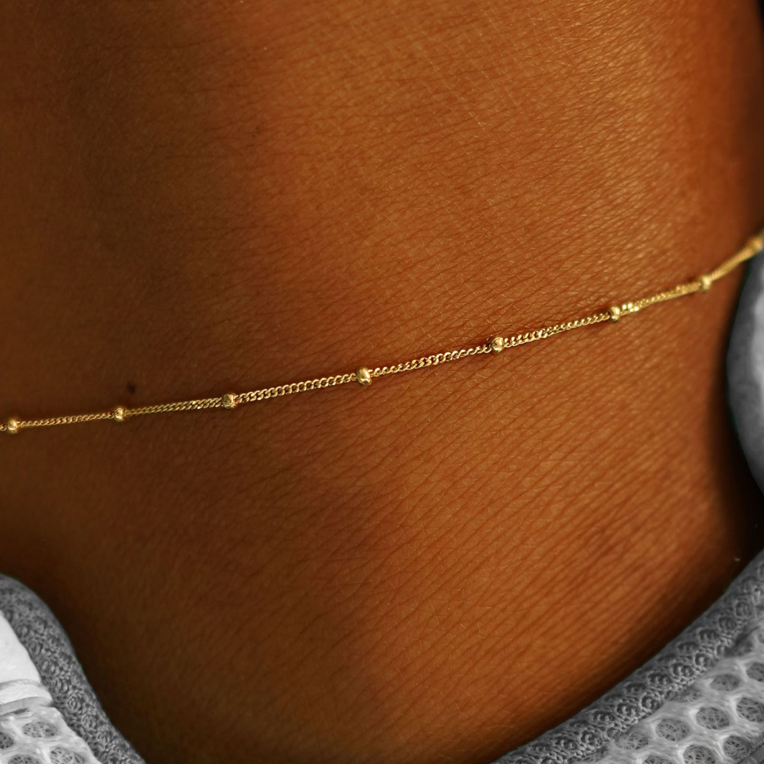 Close up view of a model's ankle wearing a yellow gold Beads Anklet