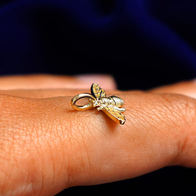 A 14k yellow gold Bee Charm for chain balancing on the back of a model's finger