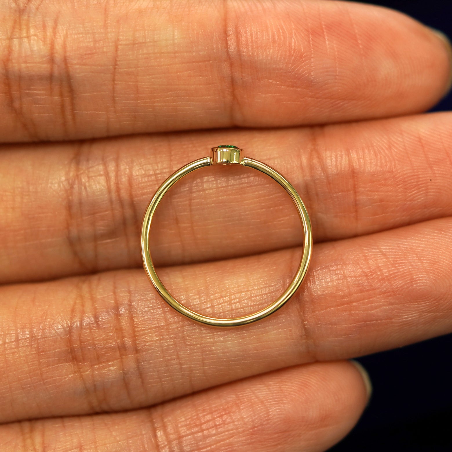 A yellow gold Emerald Ring in a model's hand showing the thickness of the band