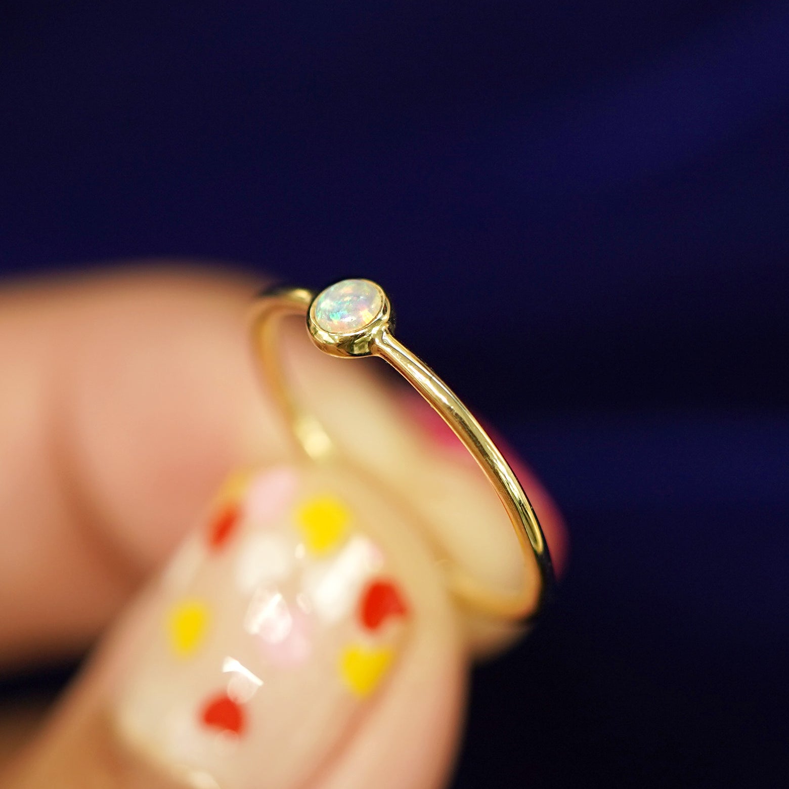 A model holding a 14k gold Opal Ring between their fingers to show the details of the bezel set stone