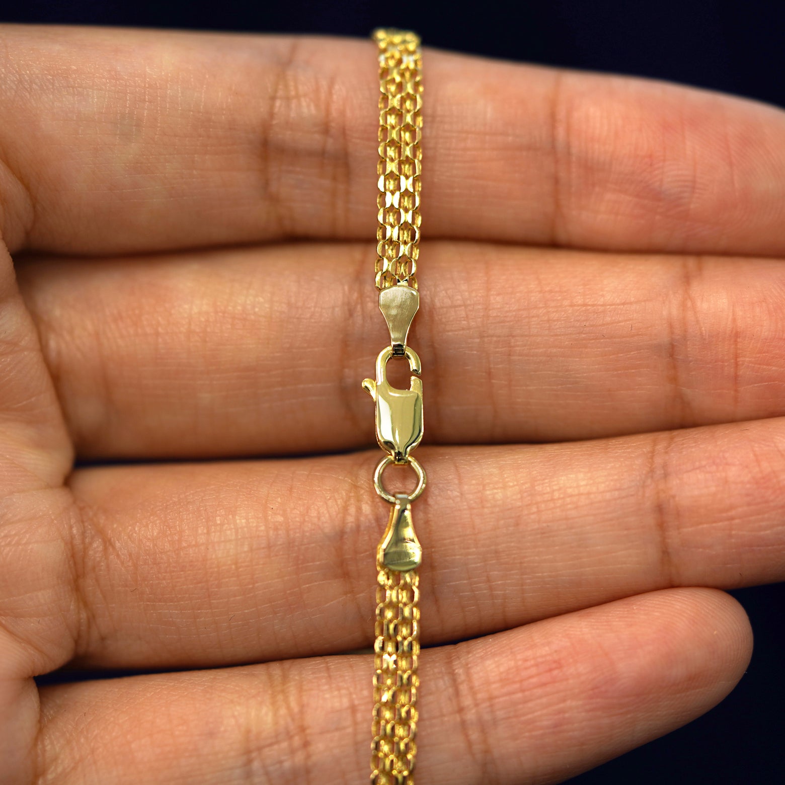 A model's hand holding a yellow 14k gold Bismarck Chain with a lobster claw clasp