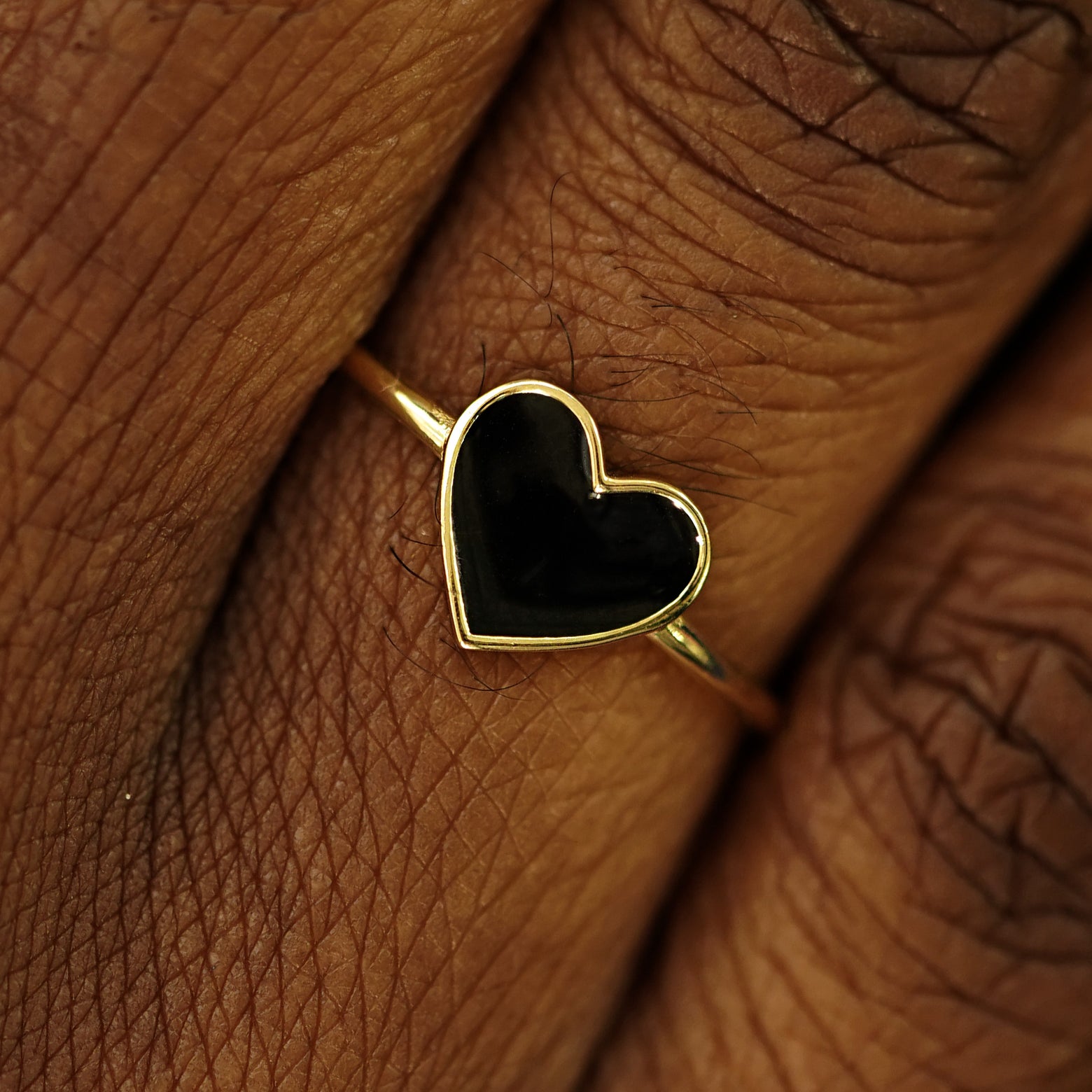 Close up view of a model's fingers wearing a 14k gold black enamel heart ring