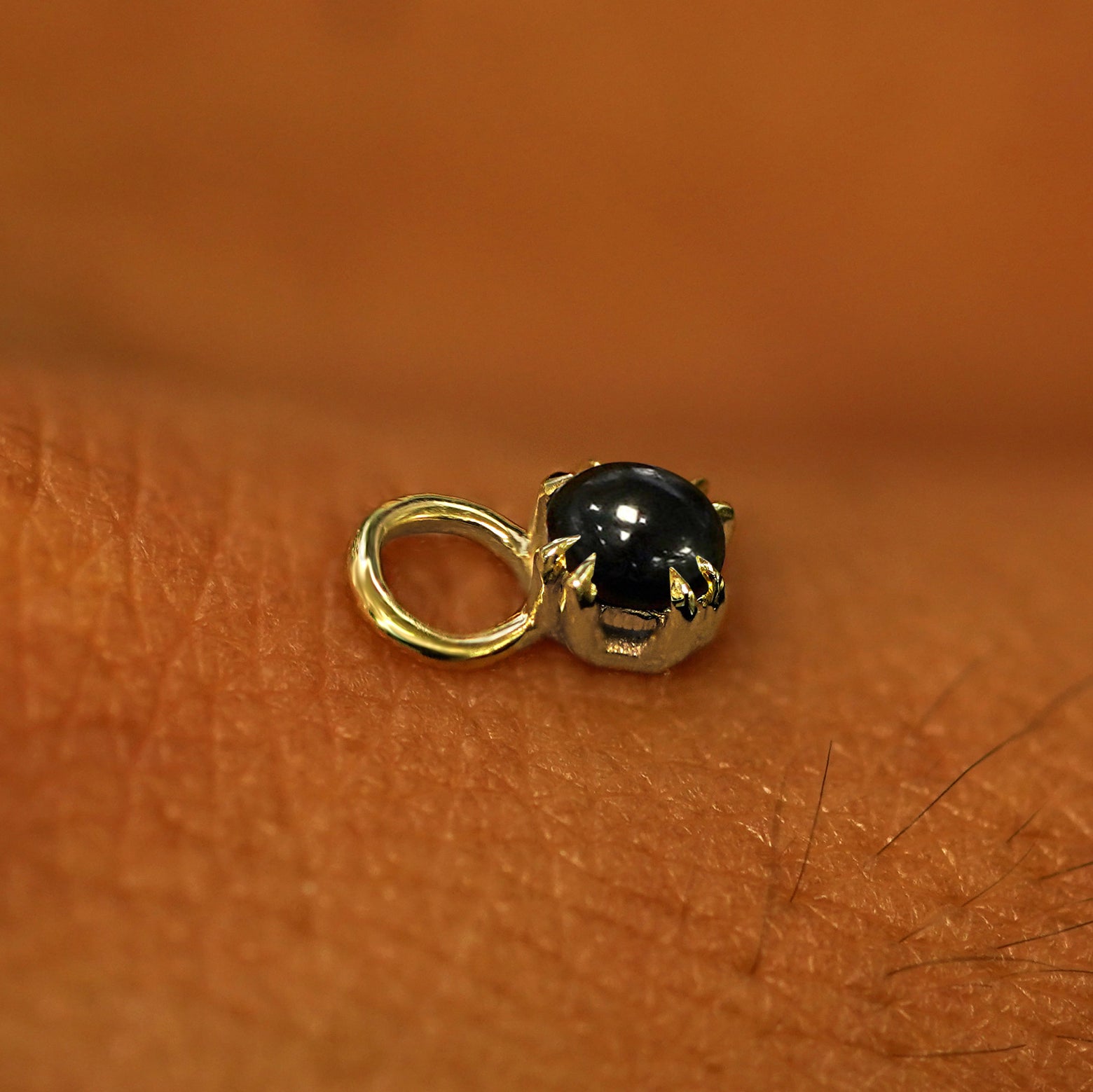 A solid yellow gold Onyx Charm for earring resting on the back of a model's hand