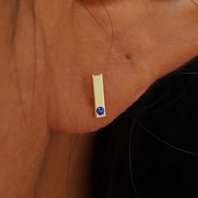 Close up view of a model's ear wearing a 14k yellow gold Sapphire Bar Earring