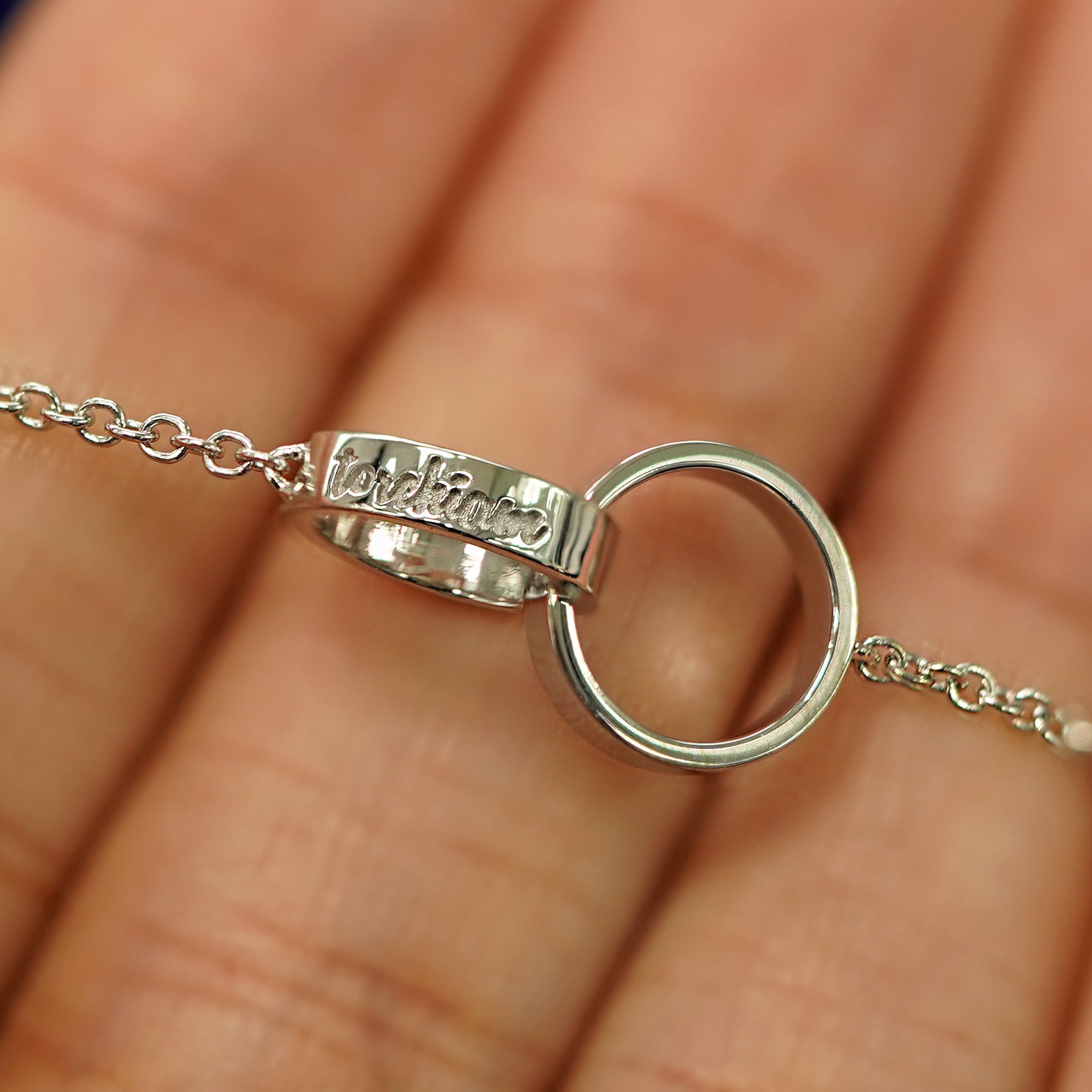 A white gold Bound Together Necklace laid across a model's fingers to show the engraving of a name on one of the rings