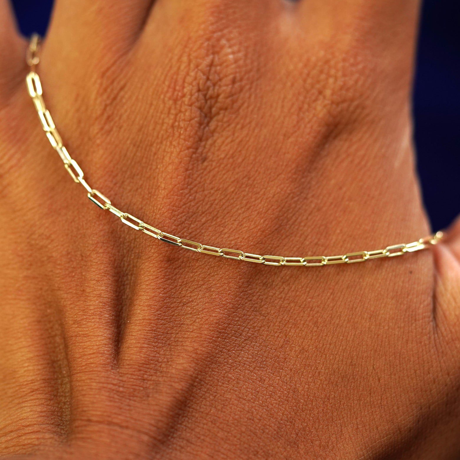 A solid gold Butch Anklet resting on the back of a model's hand