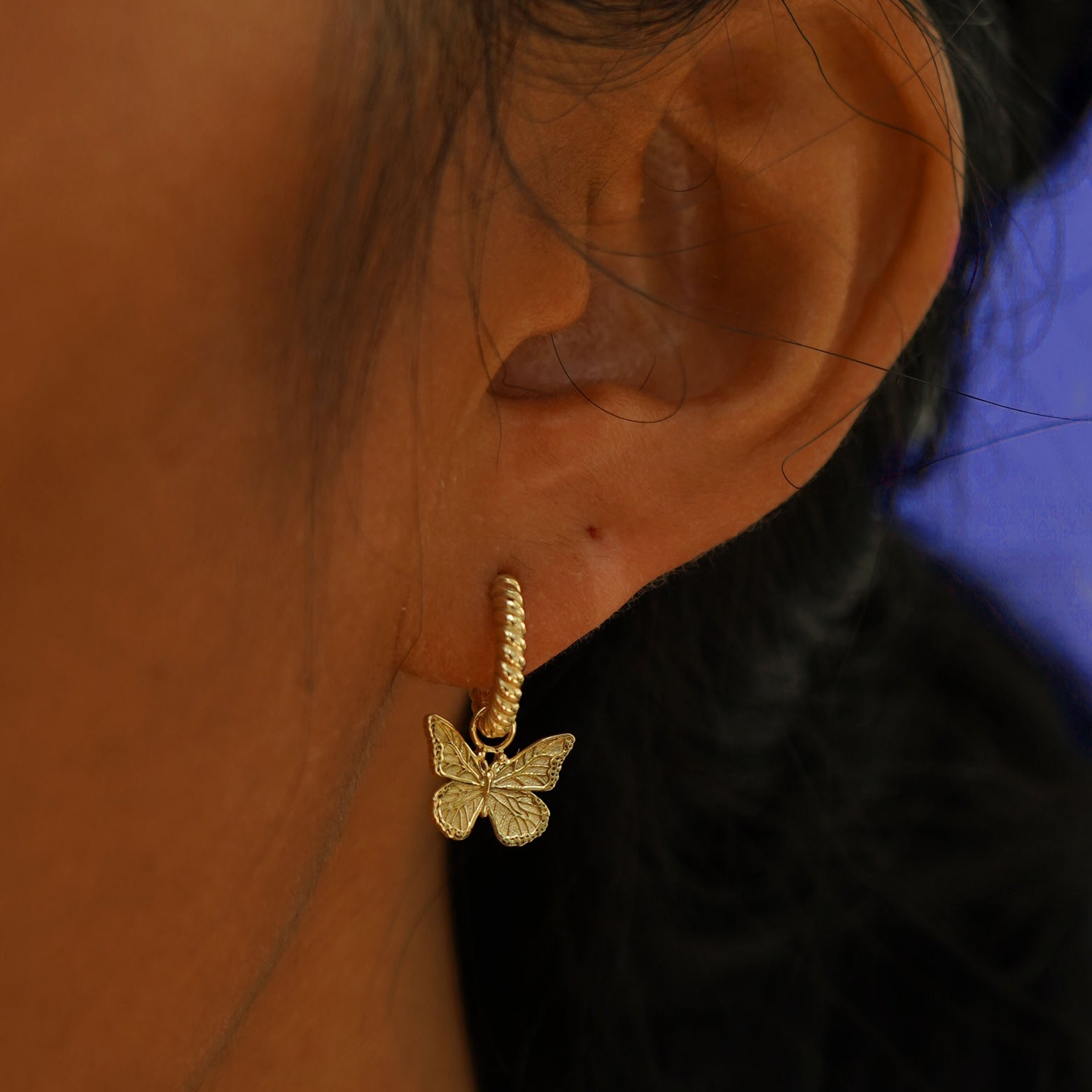 A model's ear wearing a 14k yellow gold Butterfly Charm on a Rope Huggie Earring