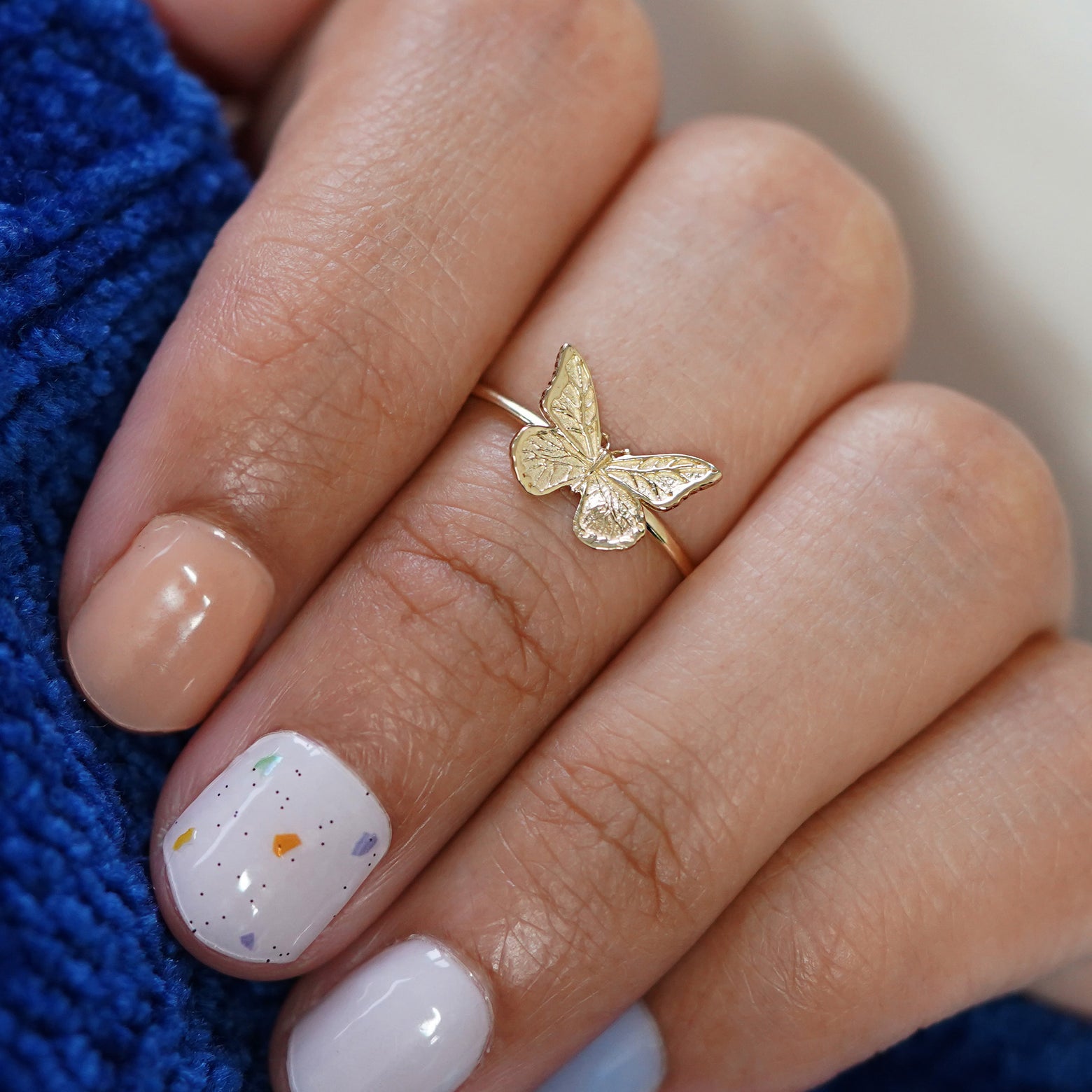 Close up view of a hand gripping a sweater wearing a Butterfly Ring as a midi ring