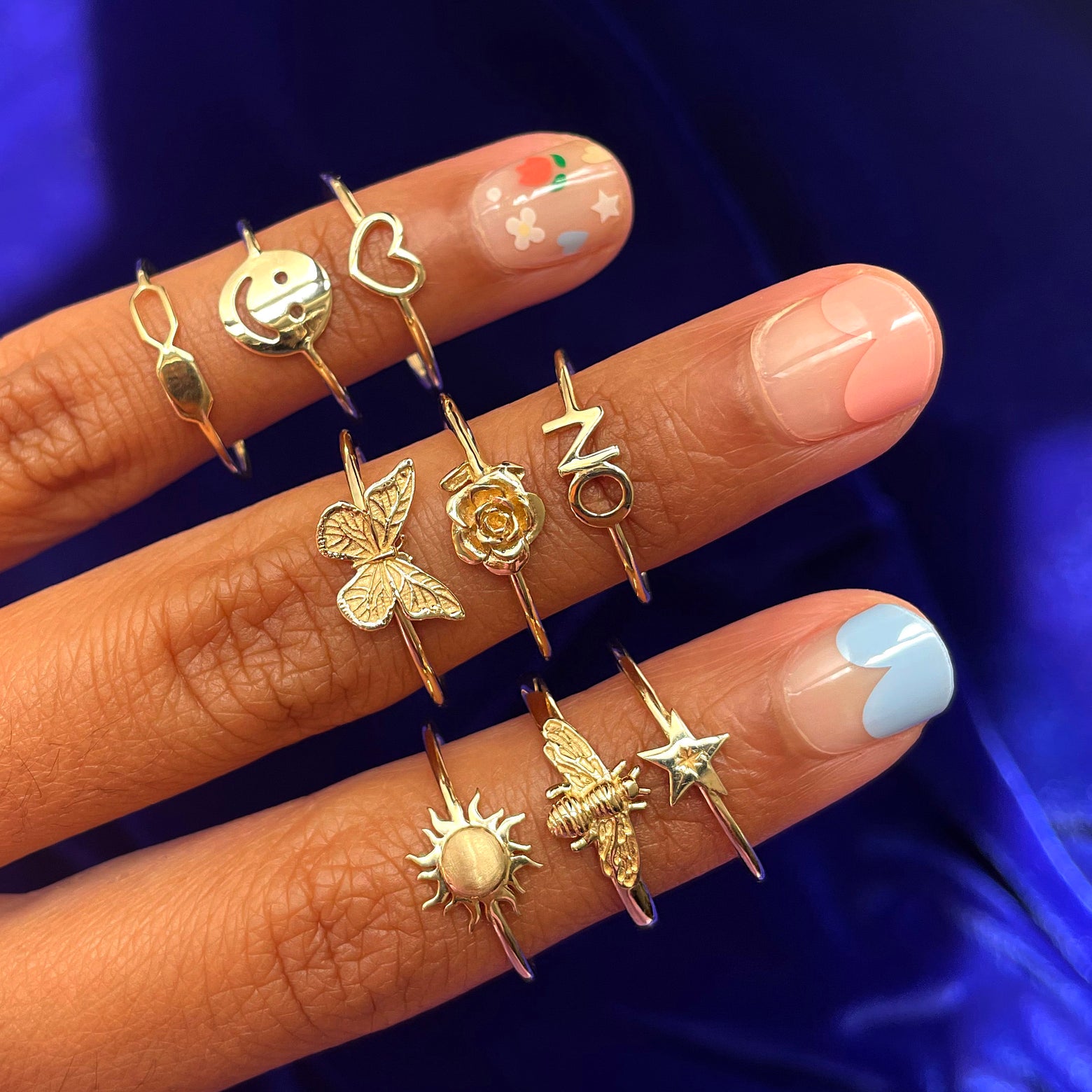 Close up view of three fingers with a colorful manicure wearing various Automic Gold rings including a Butterfly Ring