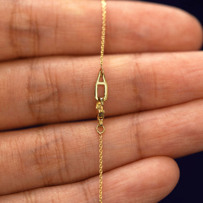 A model's hand holding an Automic Gold AU lobster claw lock on a yellow gold Cable Chain