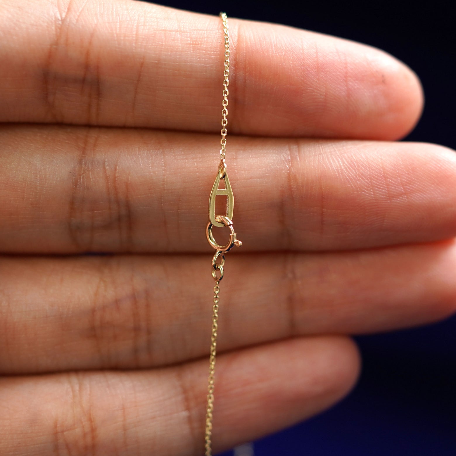 A model's hand holding an Automic Gold AU spring ring clasp on a yellow gold Cable Chain