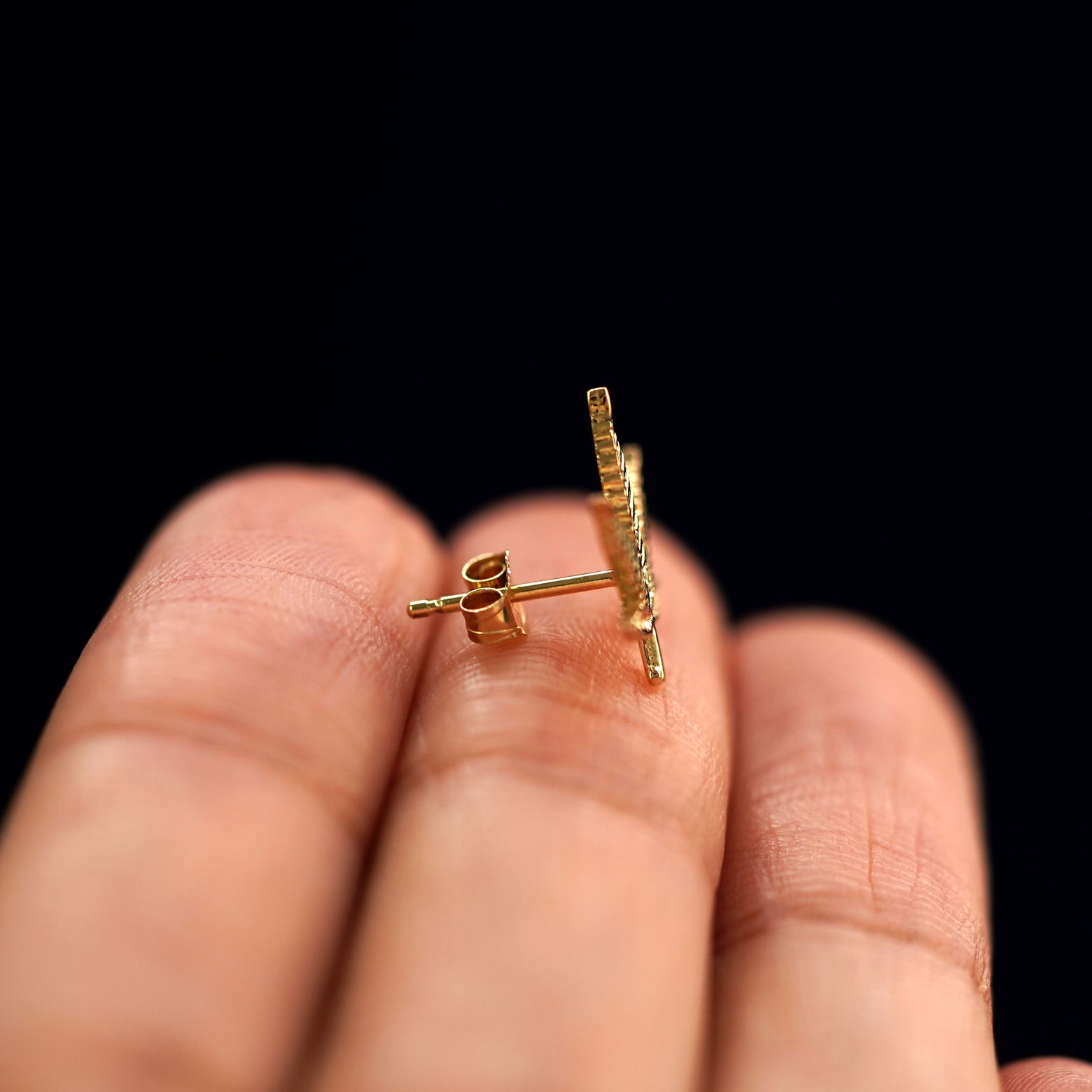 A 14k gold Cannabis Earring sitting sideways on a model's fingertips to show detail