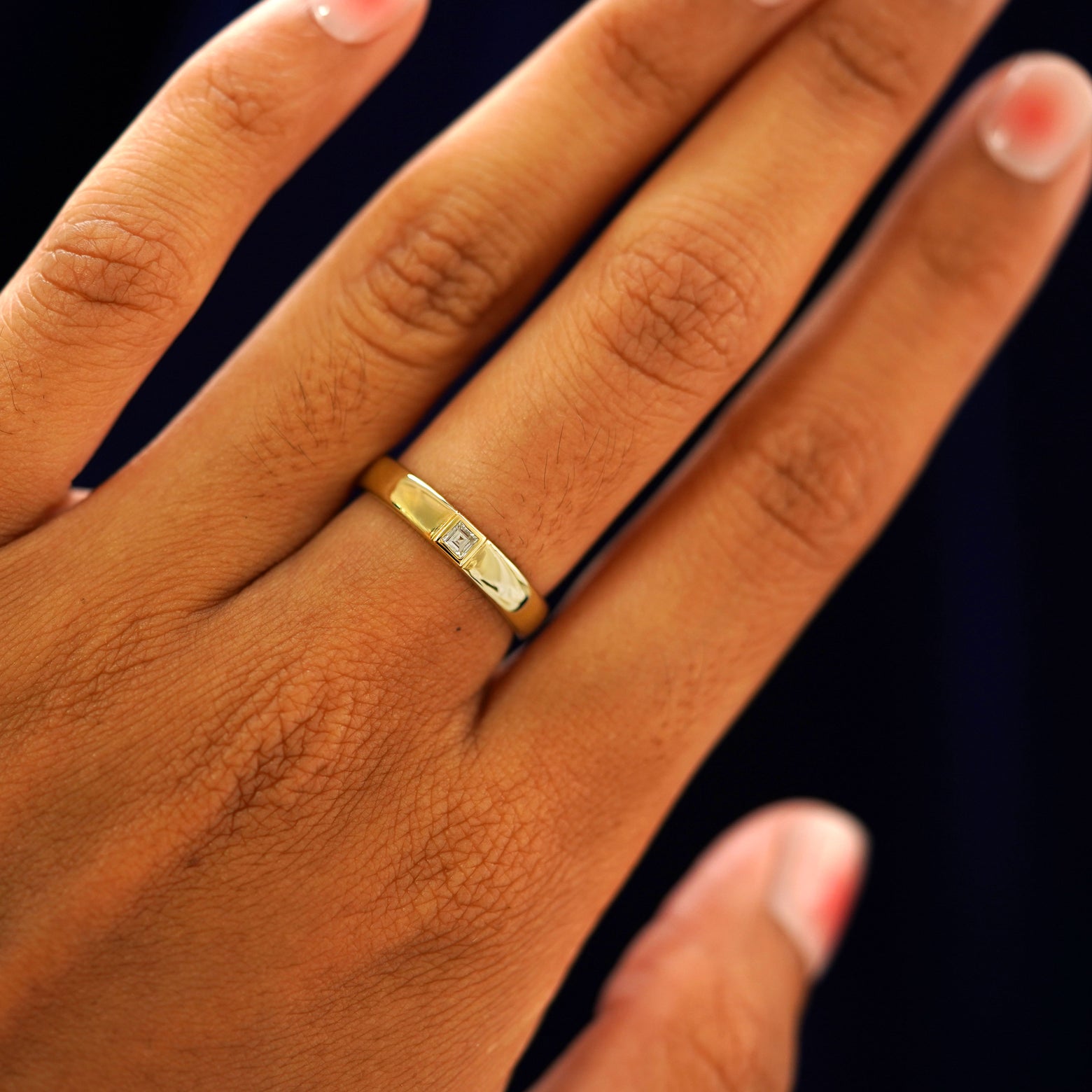 Close up view of a model's hand wearing a yellow gold Square Carre Cut Diamond Band
