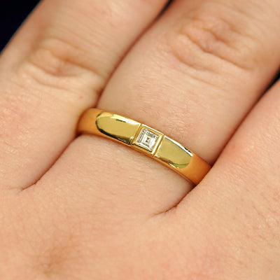 Close up view of a model's hand wearing a 14k yellow gold Square Carre Cut Diamond Band