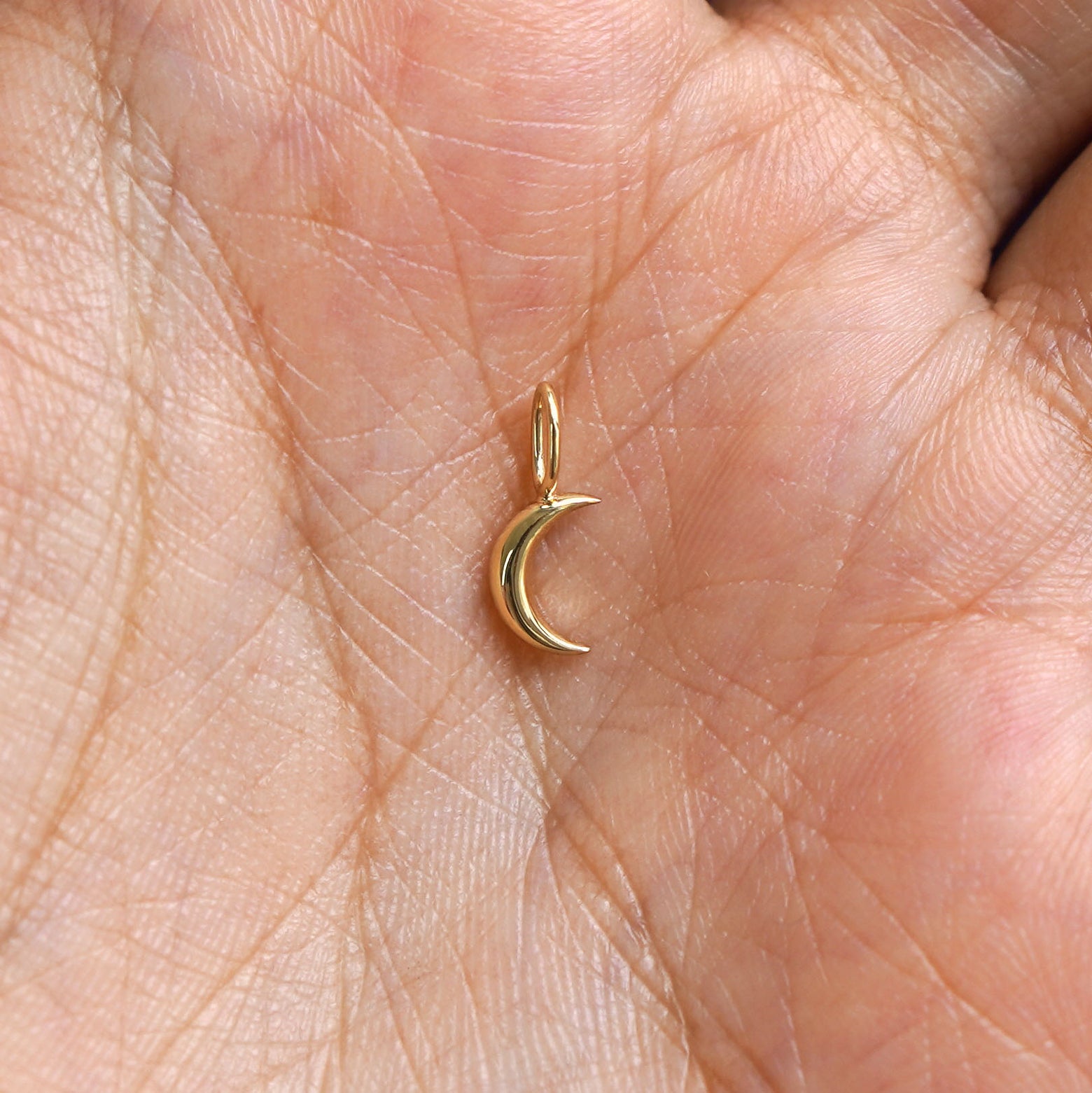 A solid gold Moon Charm for chain resting in a model's palm