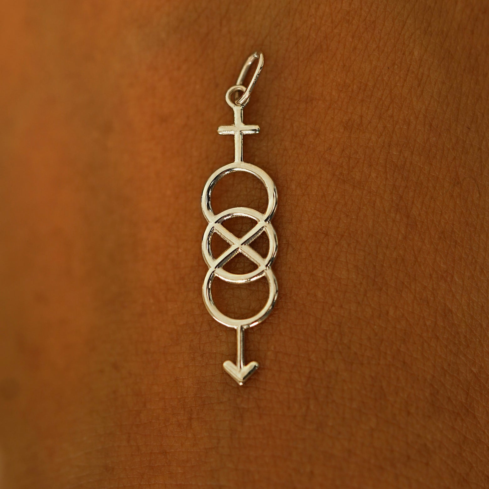 A solid 14k champagne gold Bisexual Symbol Charm resting on the back of a model's hand