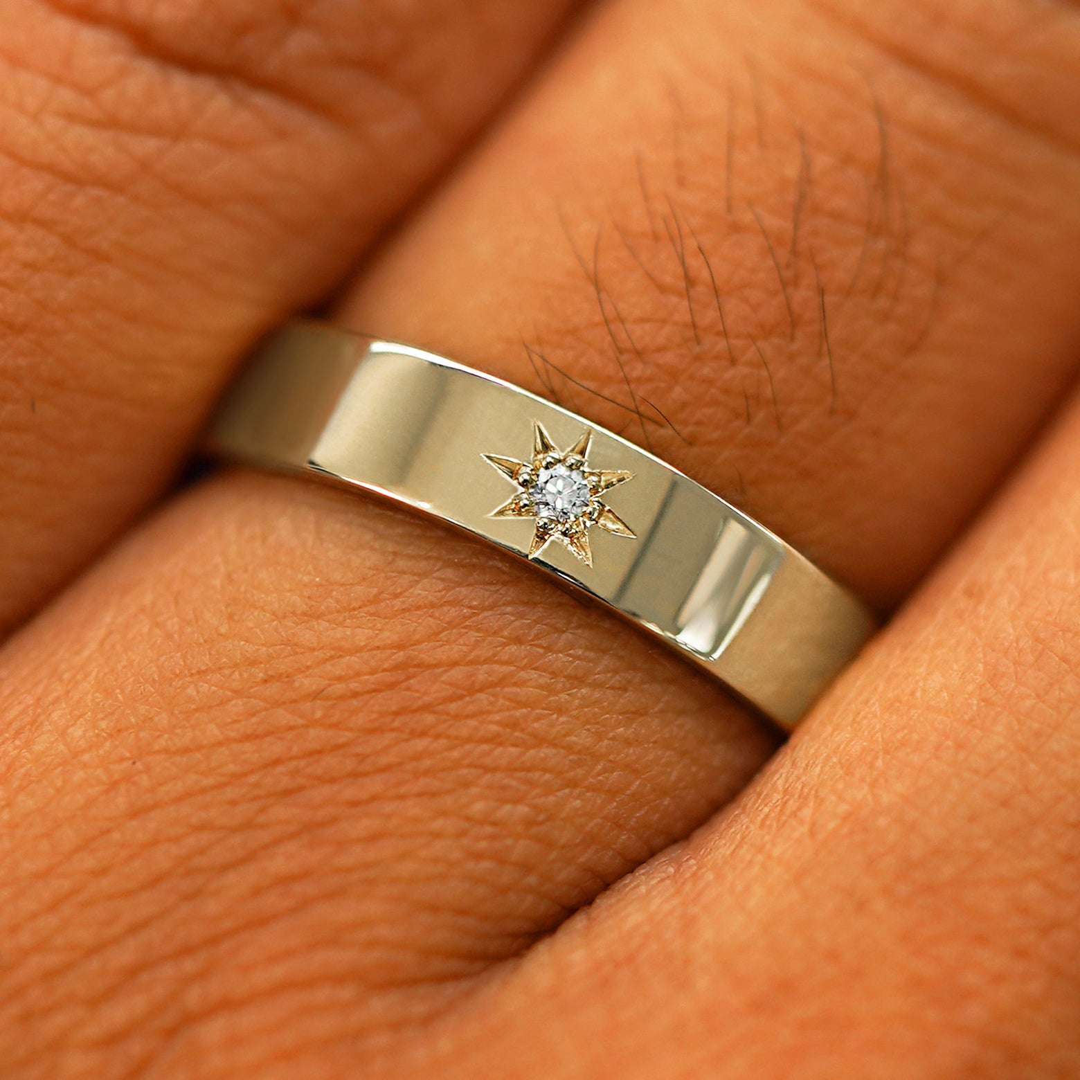 Close up view of a model's hand wearing a solid champagne gold Engraved Star Diamond Band