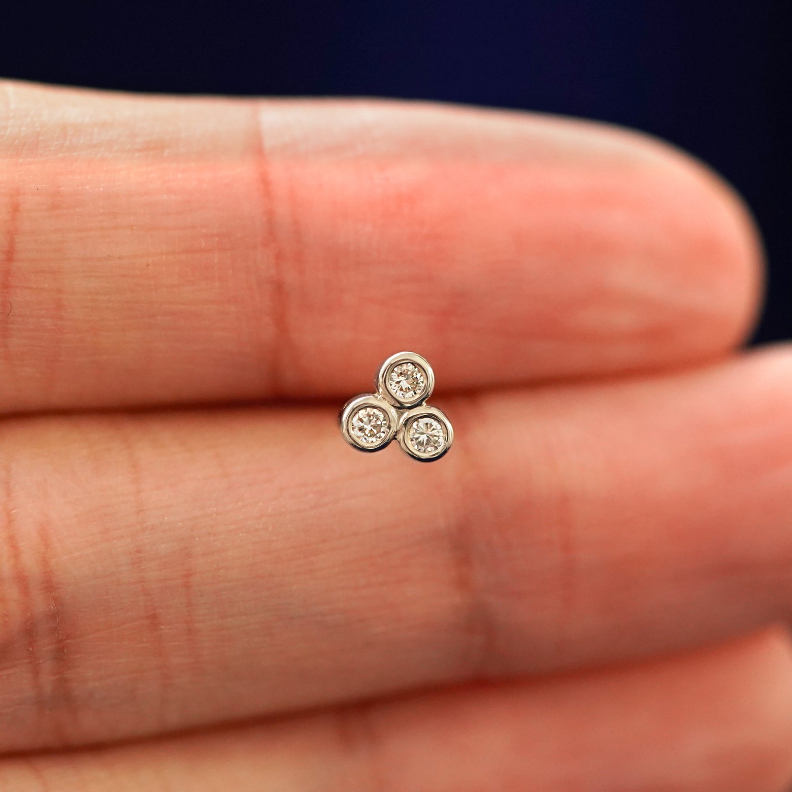 A hand holding a 14k champagne gold Diamond Trio stud Flatback Piercing in between their fingers