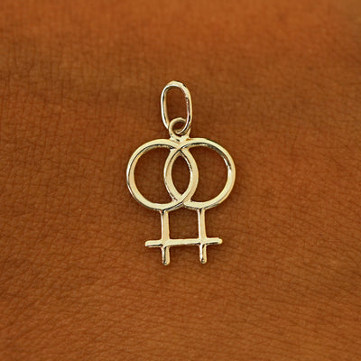 A solid 14k champagne gold Lesbian Symbol Charm resting on the back of a model's hand