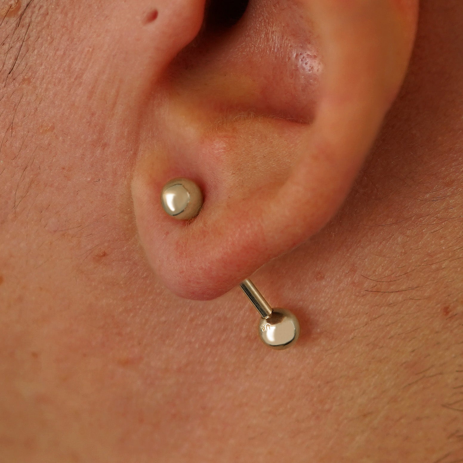 Close up view of a model's ear wearing a 14k champagne gold Medium Straight Barbell through a lobe piercing