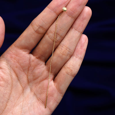 A solid 14k gold Circle Threader held between a model's fingers to show the length of the diamond cut bead chain