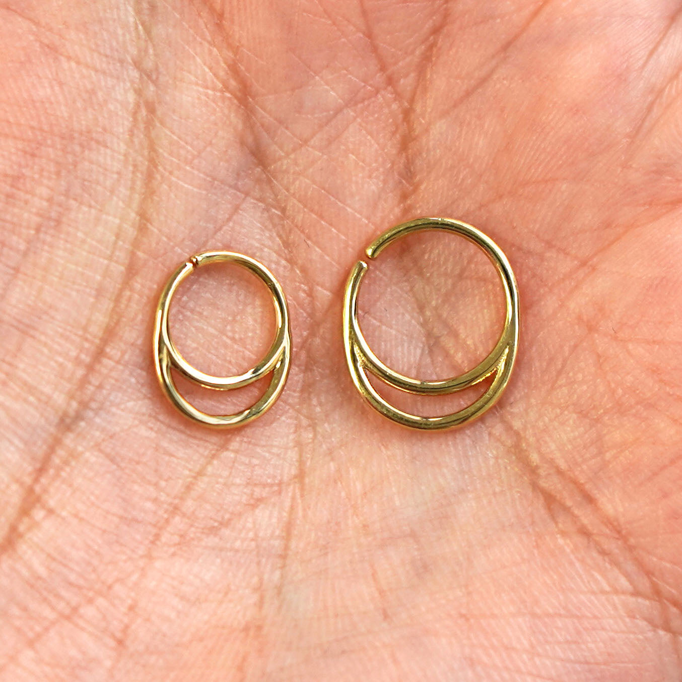 A model's palm holding two versions of the pierced Double Circle Septum showing the 8mm and 10mm sizes