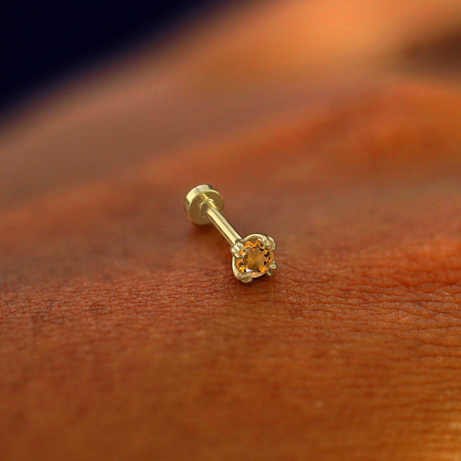 A solid 14k yellow gold Citrine Flatback Piercing resting on the back of a model's hand