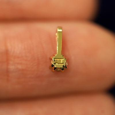 A solid gold Citrine Charm for chain facedown on a model's fingertip to show the solid back of the charm