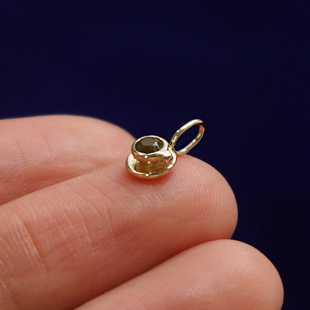 Side view of a 14k gold coffee cup charm on a model's fingertip angled to show the smoky quartz gemstone