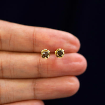 A model's hand holding a pair of recycled 14k gold Coffee Cup Earrings
