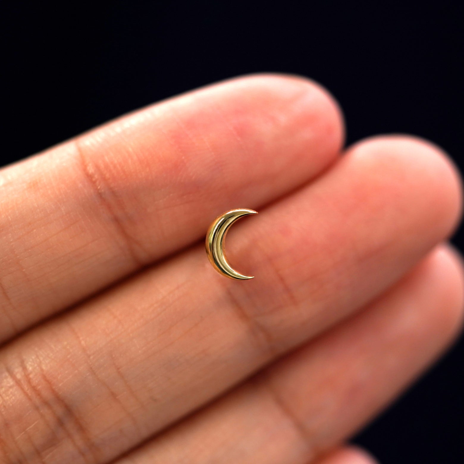 A solid 14k yellow gold Moon Earring in between a model's fingers