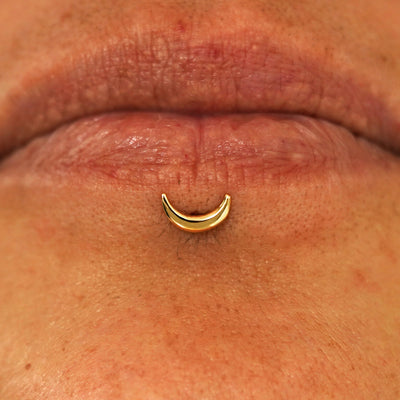 Close up view of a model's lips wearing a 14k yellow gold Moon Flatback in a labret piercing