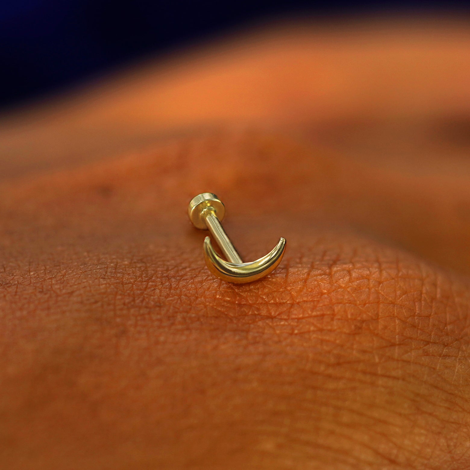 A solid 14k yellow gold Moon Flatback Piercing resting on the back of a model's hand