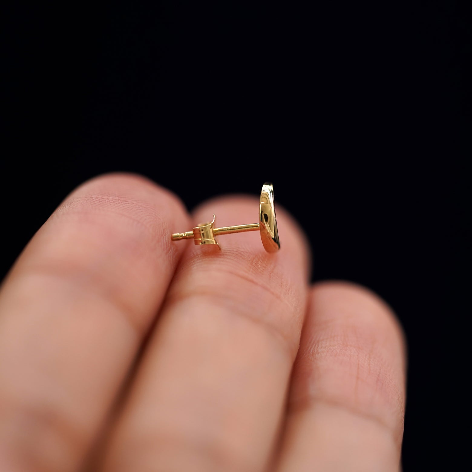 A 14k gold Moon Earring sitting sideways on a model's fingertips to show detail