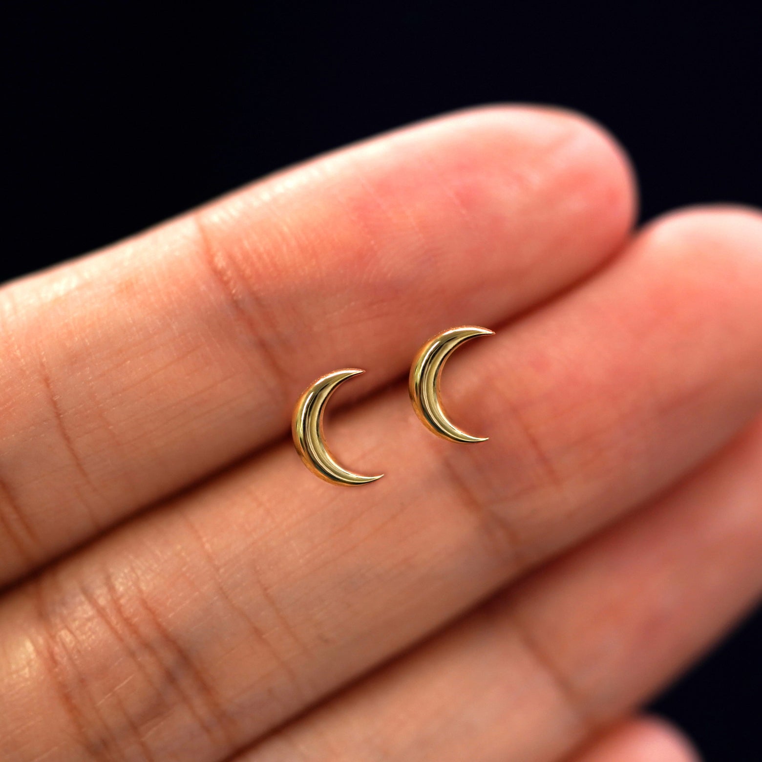 A model's hand holding a pair of recycled 14k gold Moon Earrings