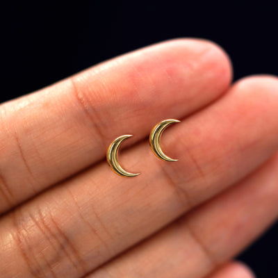 A model's hand holding a pair of recycled 14k gold Moon Earrings