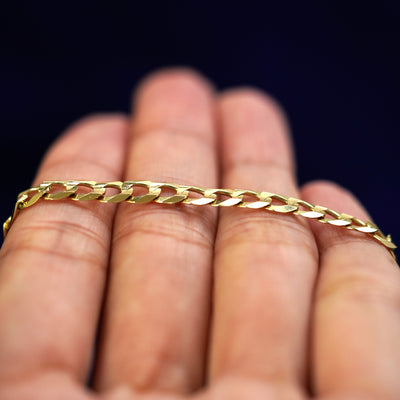 A yellow gold Curb Anklet resting on a model's fingers