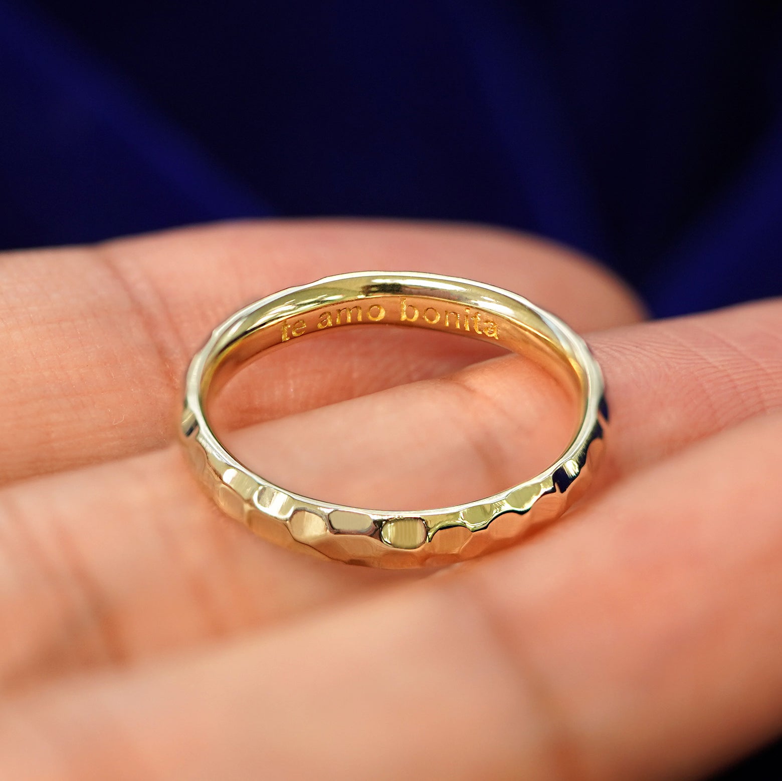A Curvy Hammered Band in a model's hand tilted to show engraving on the inside of the band that reads Te Amo Bonita