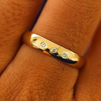 Close up view of a model's fingers wearing a 4mm yellow gold Curvy Mirror Band with three diamonds