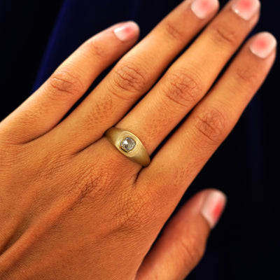 Close up view of a model's hand wearing a yellow gold Cushion Salt and Pepper Diamond Signet Ring on their finger