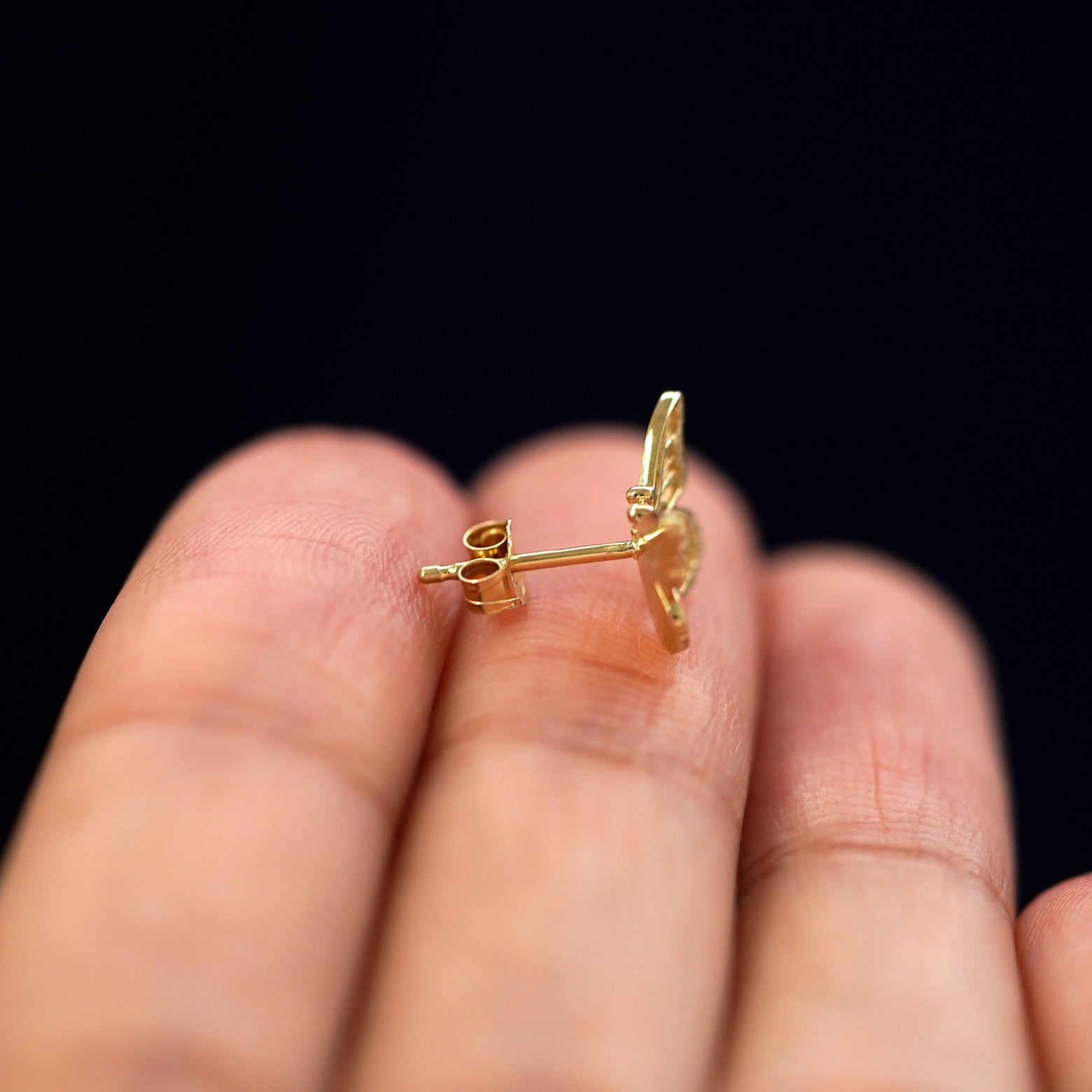 A 14k gold Butterfly Earring sitting sideways on a model's fingertips to show detail