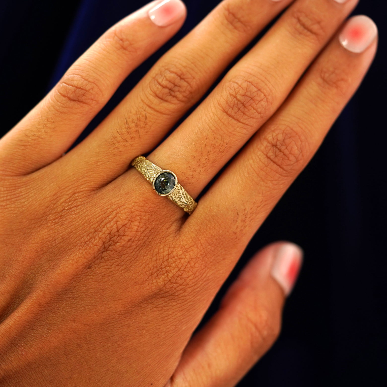 Close up view of a model's hand wearing a yellow gold Dark Green Sapphire Pine Ring on their finger