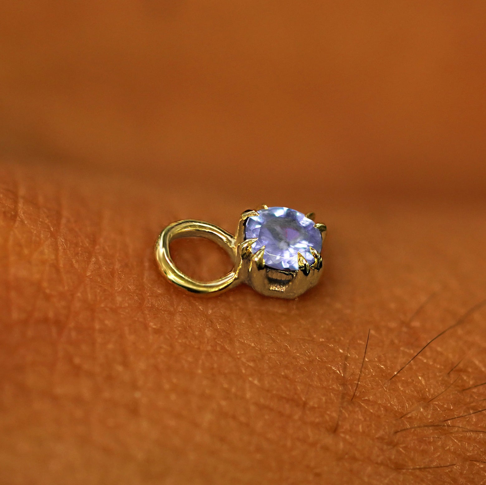 A solid yellow gold Tanzanite Charm for earring resting on the back of a model's hand