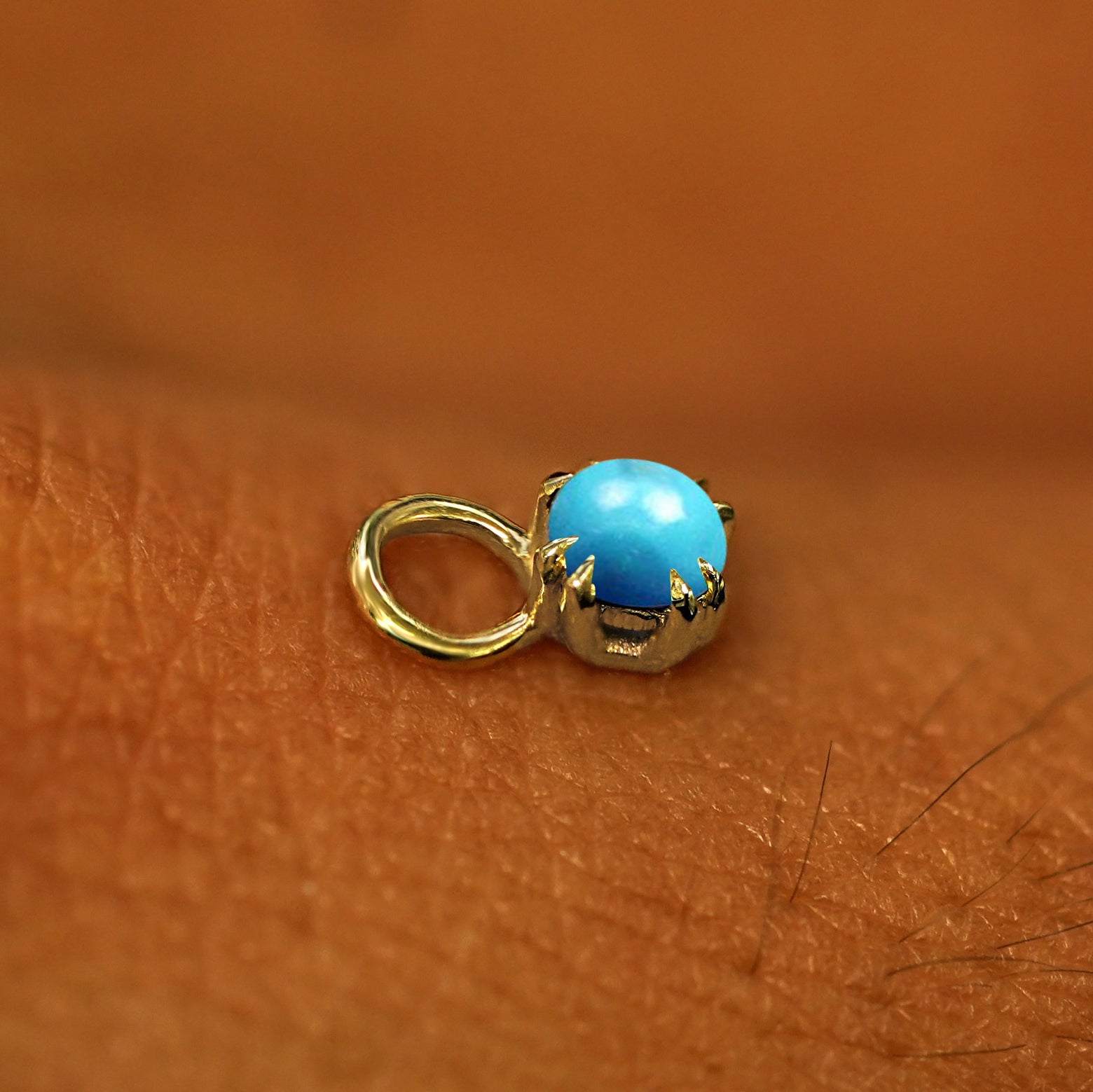 A solid yellow gold Turquoise Charm for earring resting on the back of a model's hand