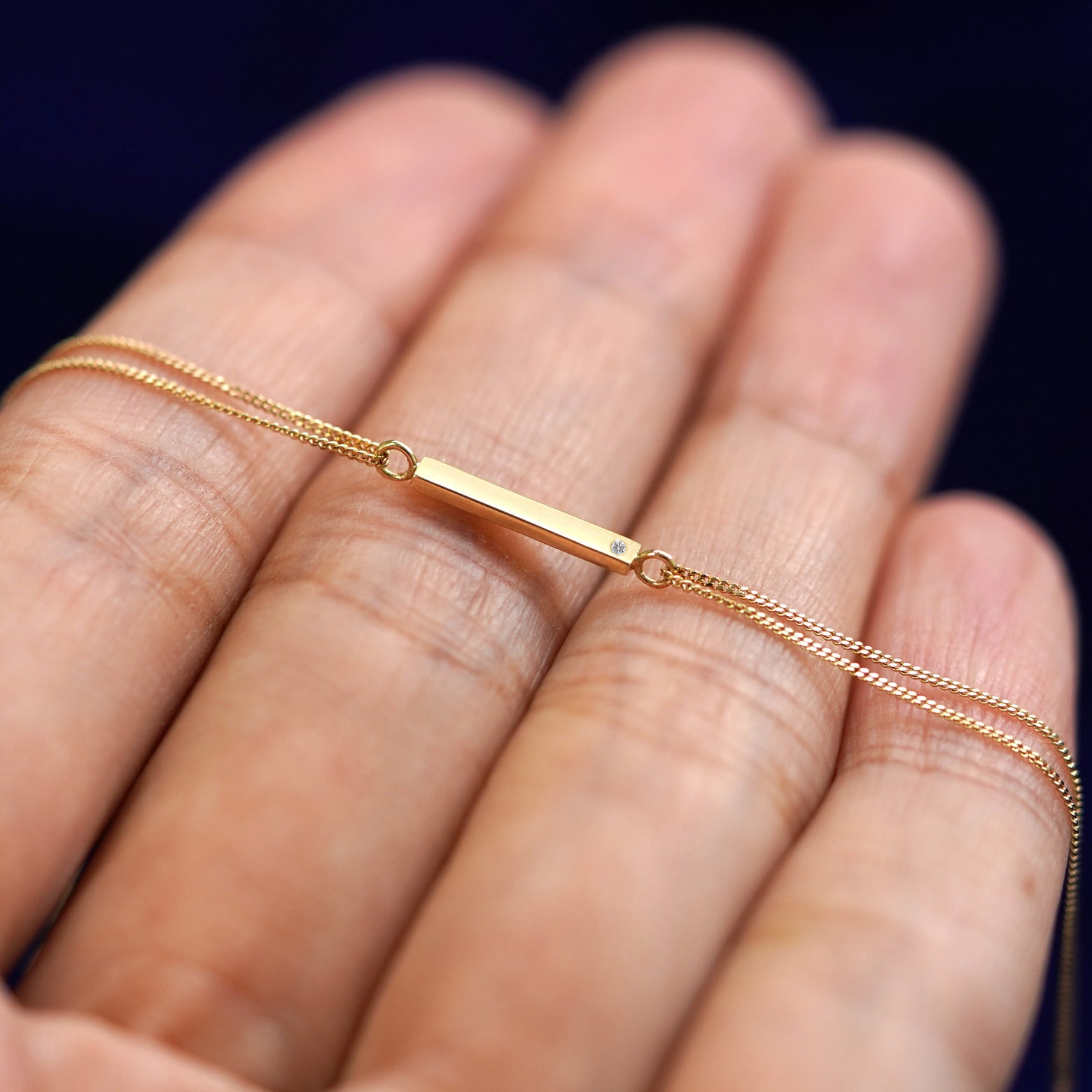 A yellow gold diamond Gemstone Bar Bracelet resting on a model's fingers