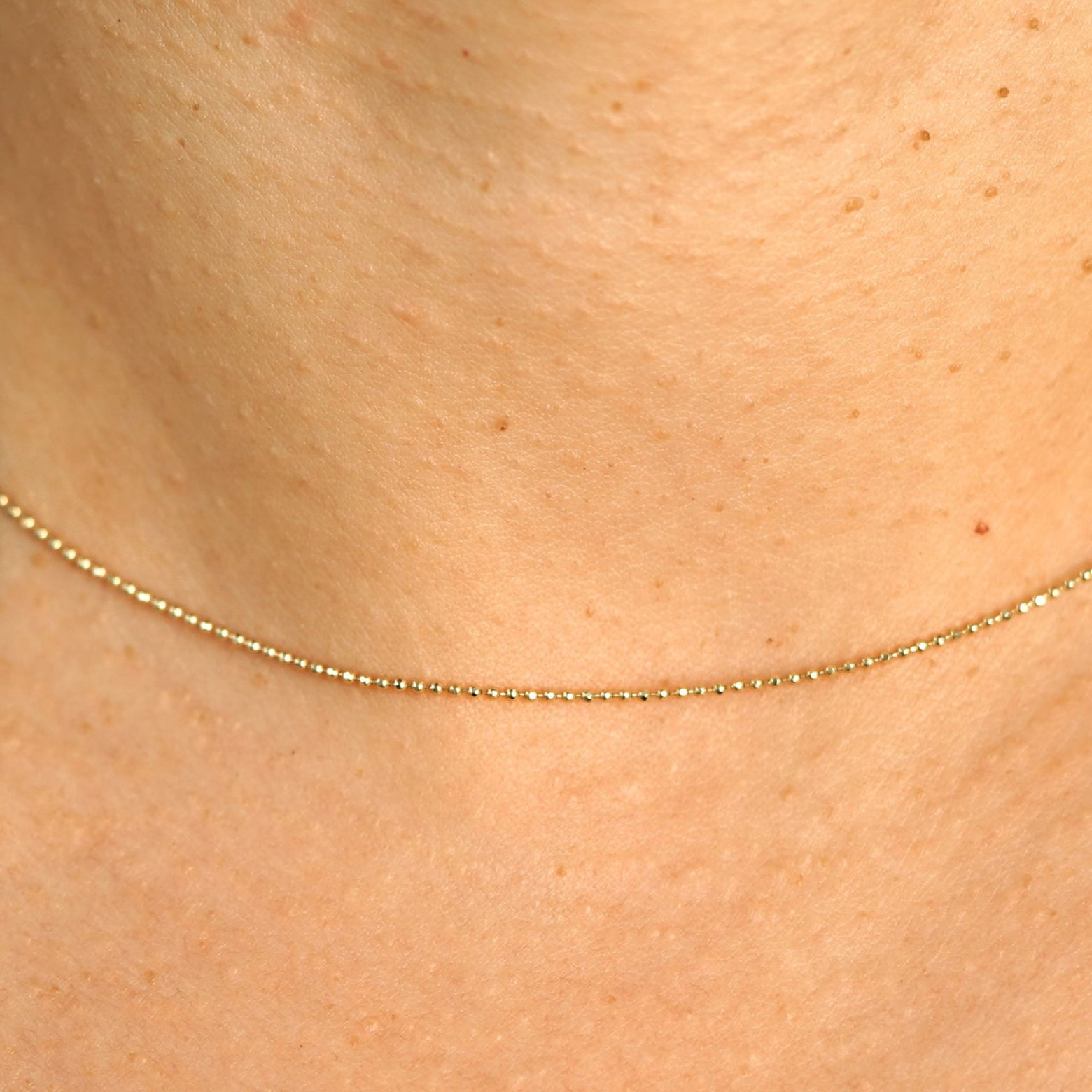 Close up view of a model's neck wearing a solid yellow gold Bead Chain