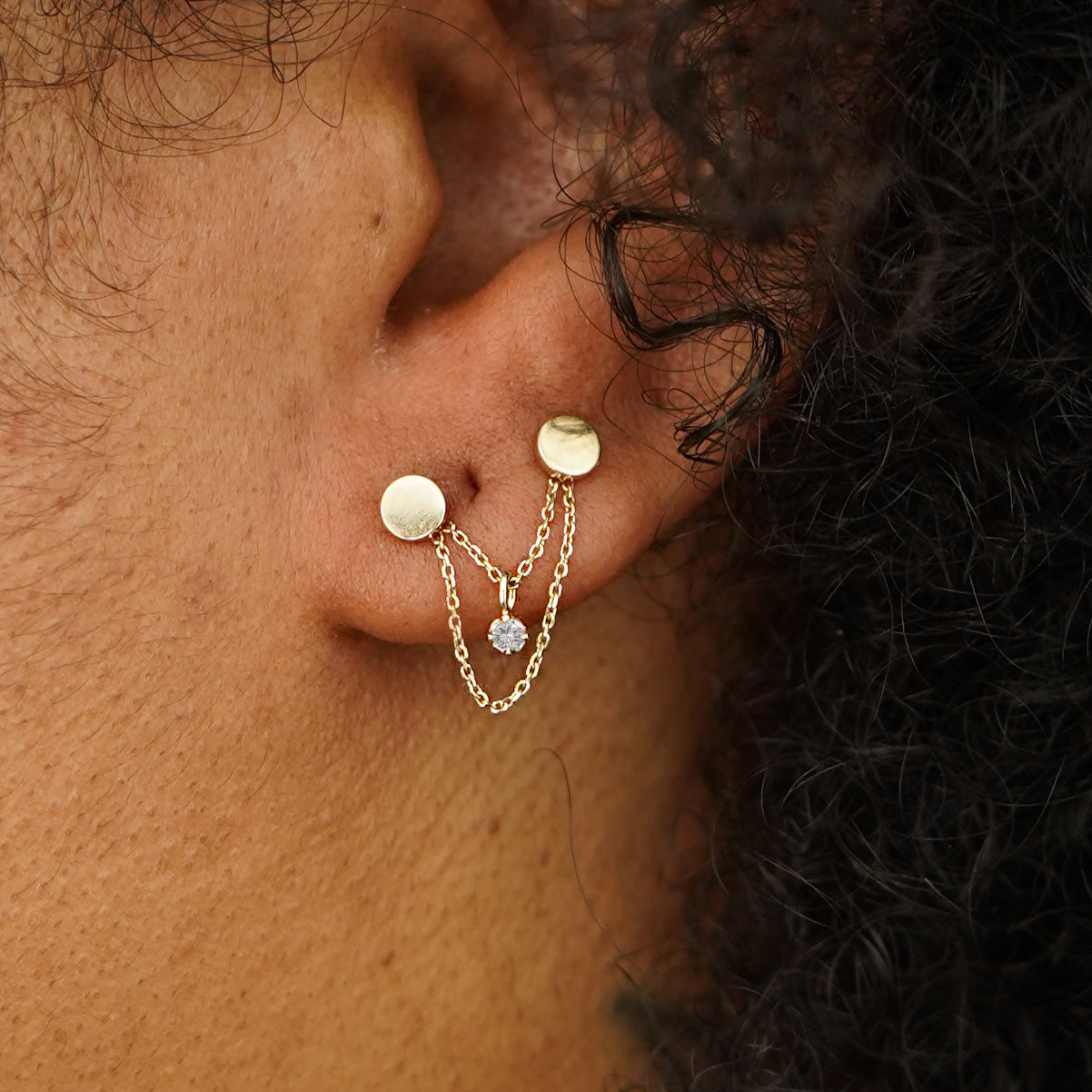 A model's ear wearing a yellow gold Diamond Cable Chain Connector across two Circle Studs on their lobe