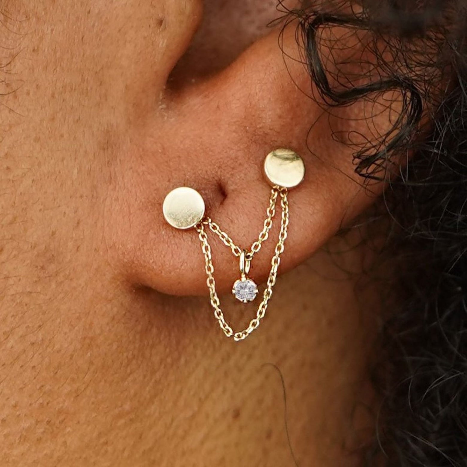 Close up view of a model's ear wearing a yellow gold Diamond Cable Chain Connector across two Circle Studs on their lobe